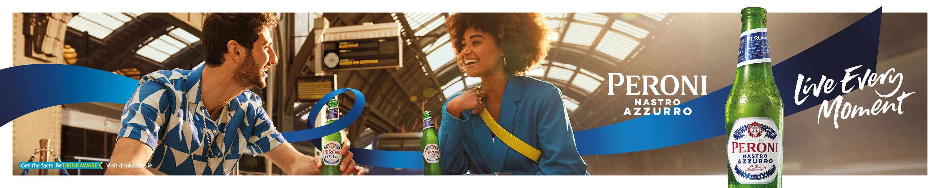 A couple at a train station enjoying bottles of Peroni Nastro Azzurro. Tag line: Live every moment.